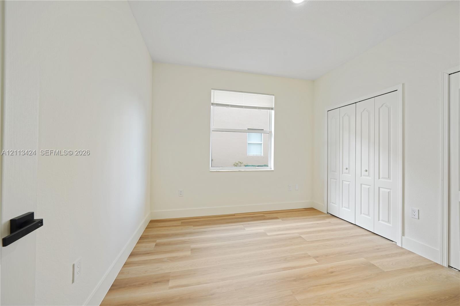 Room featuring neutral wall paint, wood-finish flooring, a single window, and a built-in closet with four-panel bi-fold doors