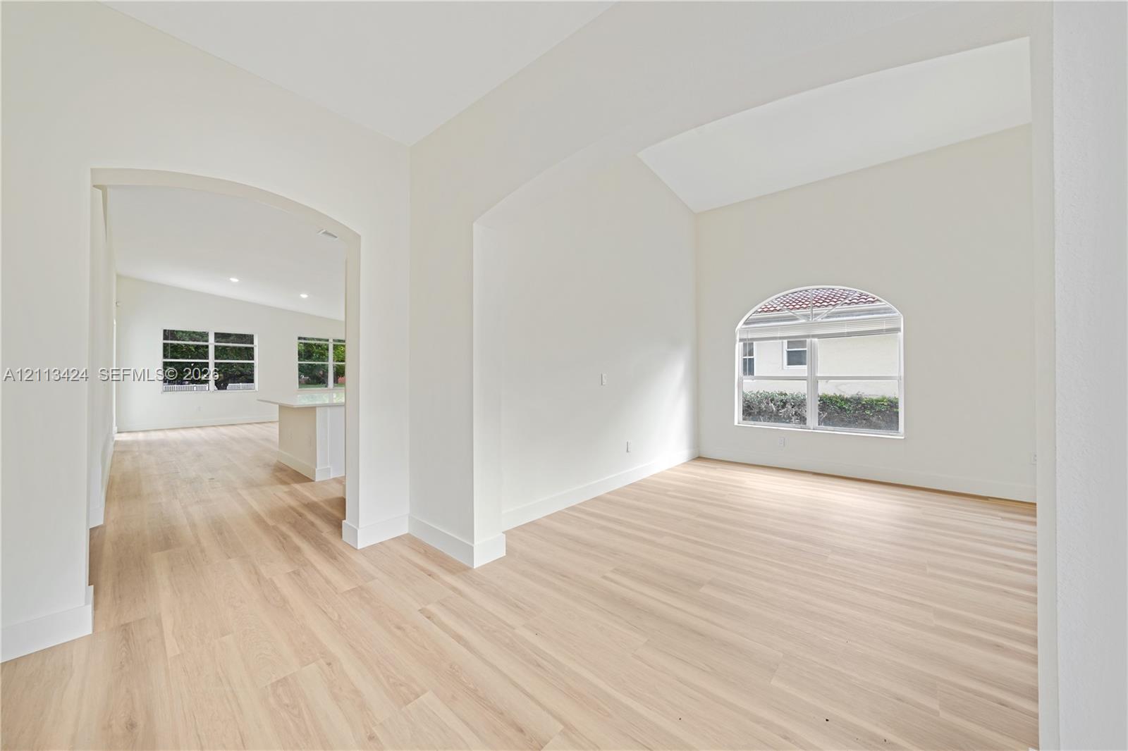 Interior space featuring vaulted ceilings, wood-finish flooring, an arched window, and architectural arched openings