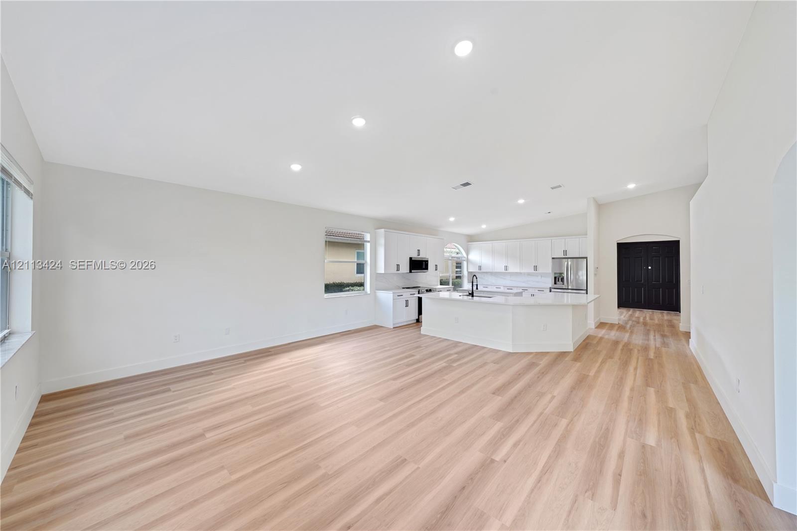 Open concept kitchen and living area featuring wood-finish flooring, white cabinetry, quartz countertops, a central island, and recessed lighting