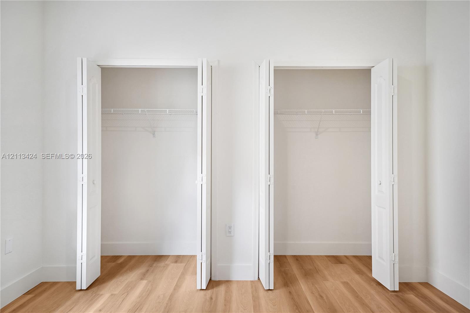Dual closets featuring white bi-fold doors and integrated wire shelving, complemented by wood-finish flooring