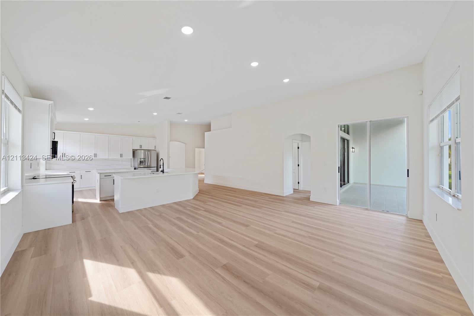 Open-concept kitchen featuring white cabinetry, a center island with quartz countertops, wood-finish flooring, recessed lighting, and sliding glass doors