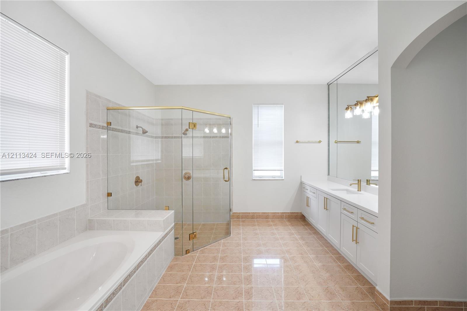 Bathroom featuring a glass-enclosed shower, soaking tub with tile surround, dual-sink vanity with white cabinetry, and large-format wall mirror