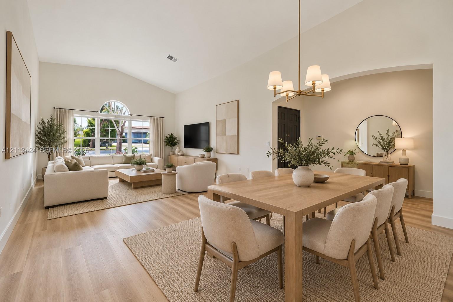 virtually staged Open-concept living space featuring vaulted ceilings, wood-finish flooring, a multi-pane window with an arched transom, and an overhead multi-arm chandelier