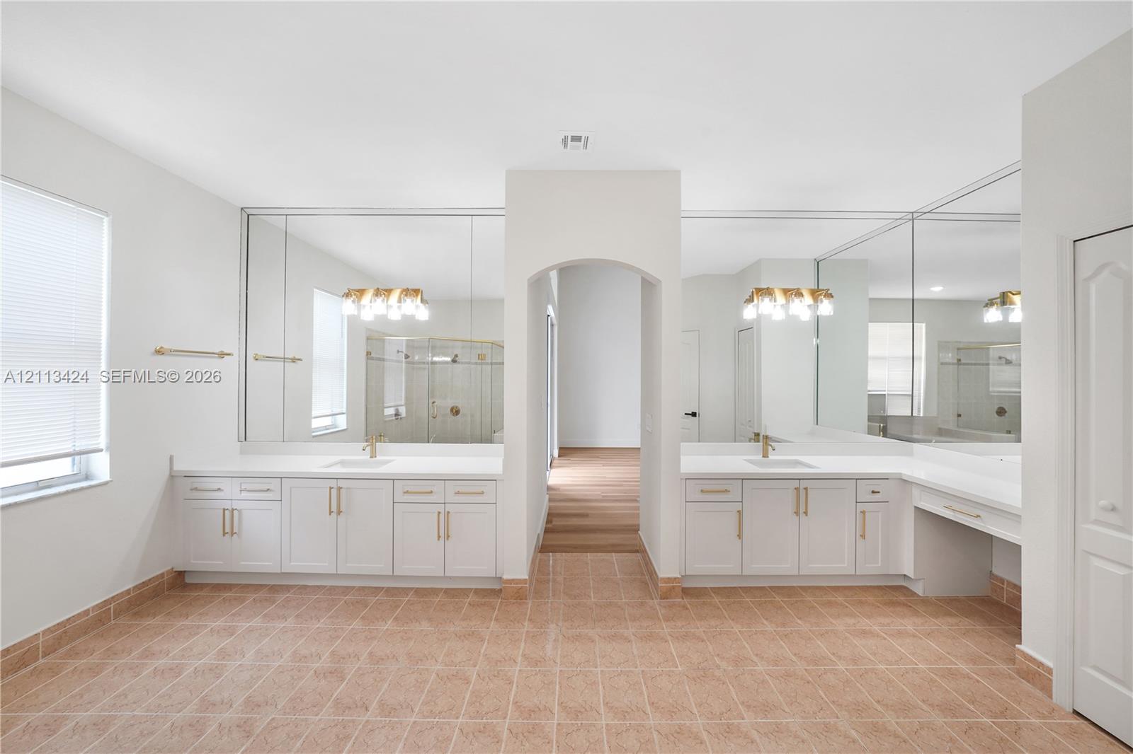 Dual-vanity cabinetry with white countertops, integrated sinks, brass-finish hardware, full-width vanity mirrors, and ceramic tile flooring