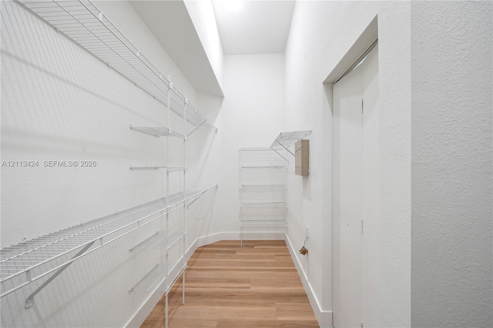 Walk-in closet featuring wood-finish flooring, white walls, vaulted ceiling, and tiered white wire shelving