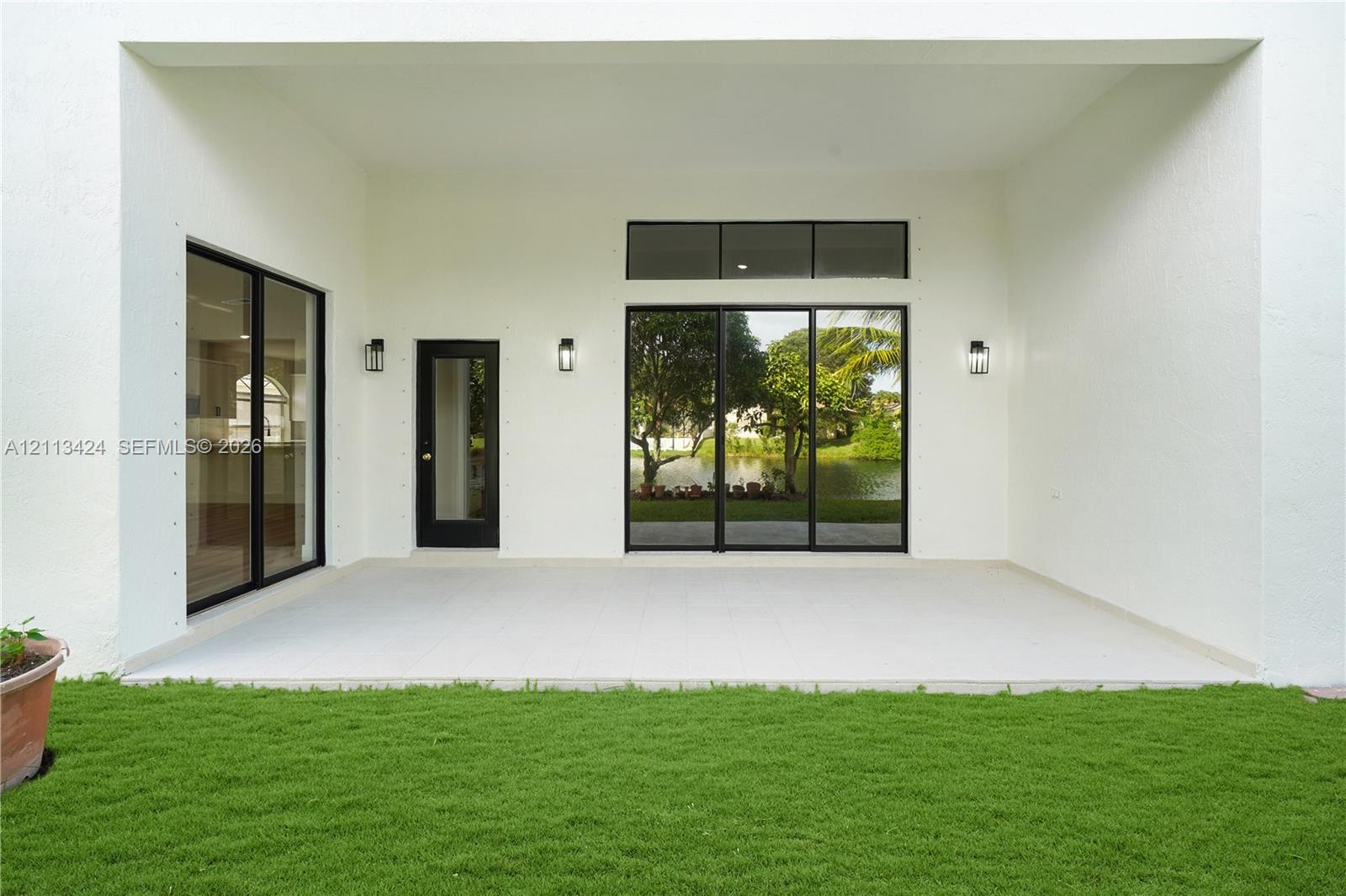 Covered patio featuring large-format tile flooring, multi-panel sliding glass doors, a transom window, and wall-mounted exterior lighting