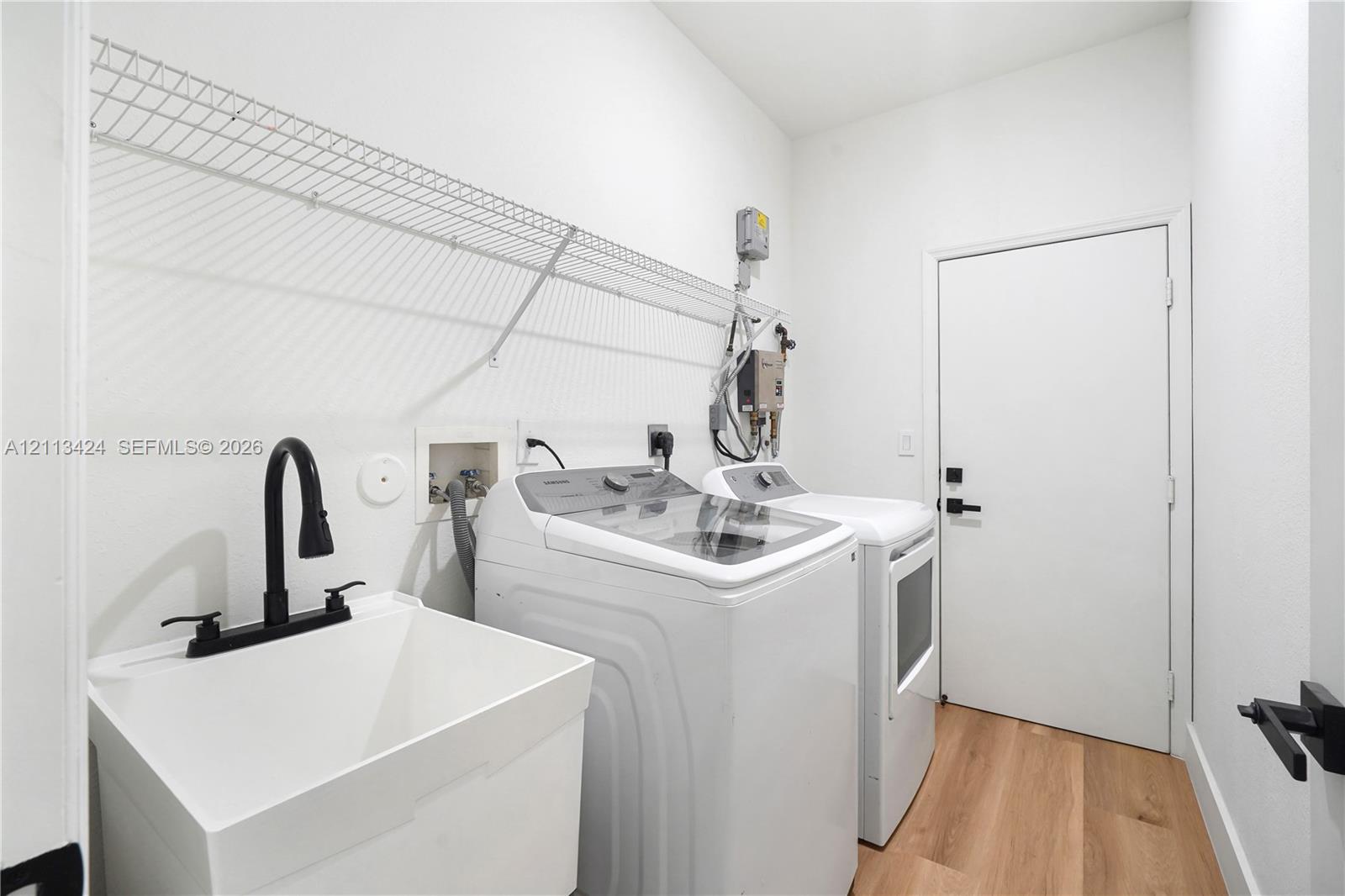 Laundry room featuring wood-finish flooring, a utility sink with a matte black faucet, and an integrated wire wall shelf