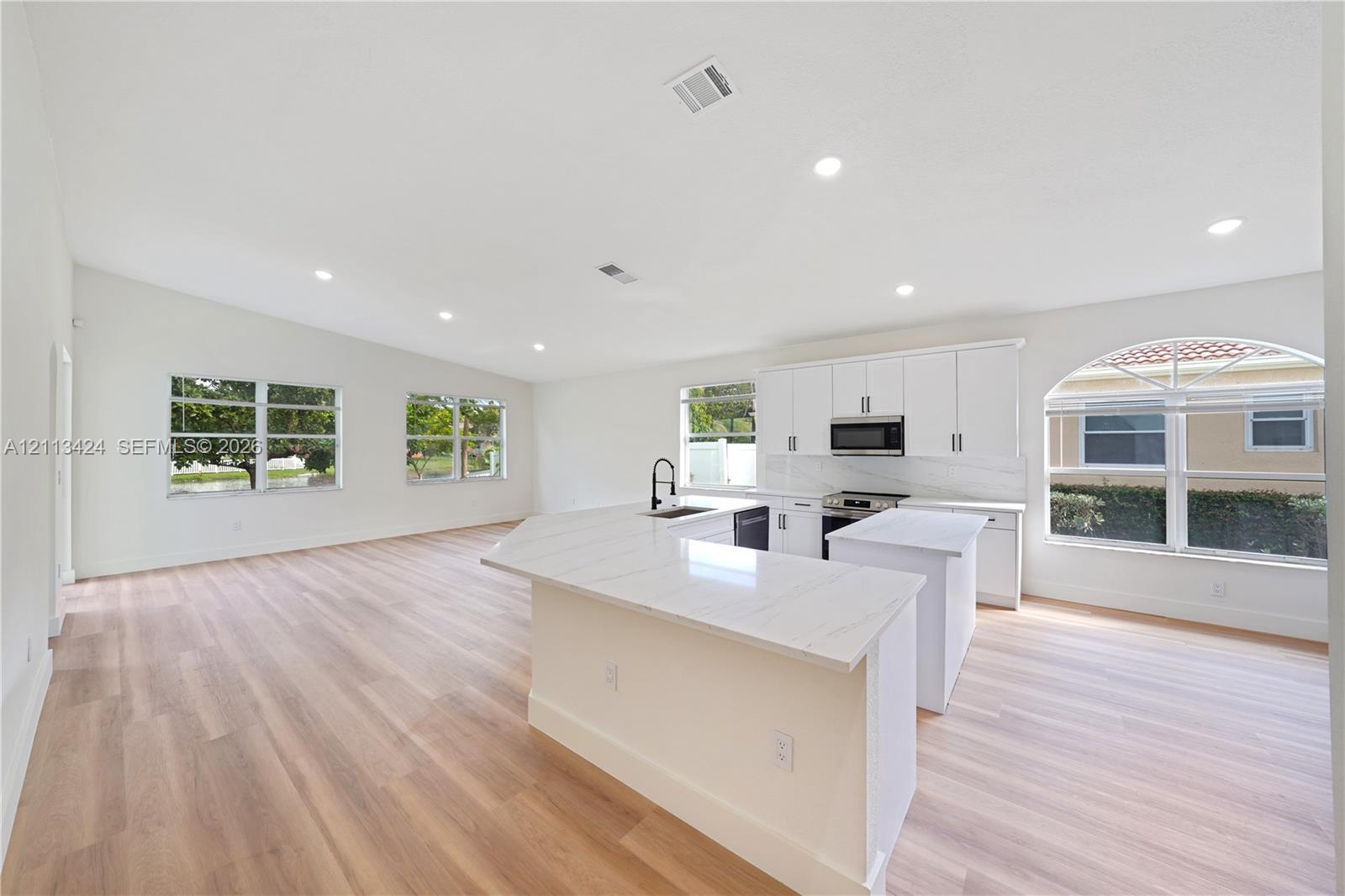 Open-concept kitchen and living area featuring wood-finish flooring, a quartz-topped peninsula, recessed lighting, white cabinetry, and an arched window