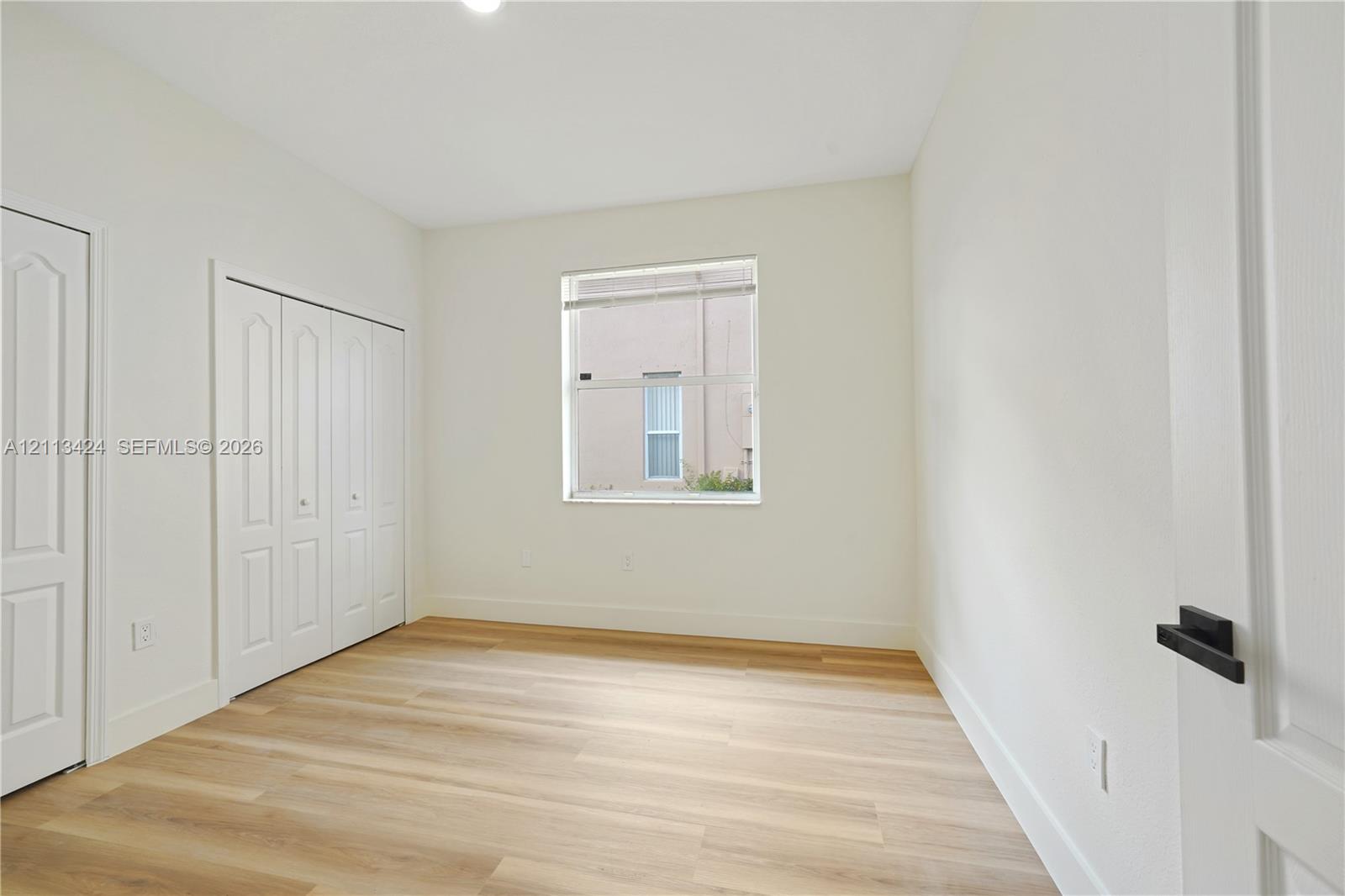 Neutral-toned interior featuring wood-finish flooring, a single-hung window, and a multi-panel closet door with matte black hardware