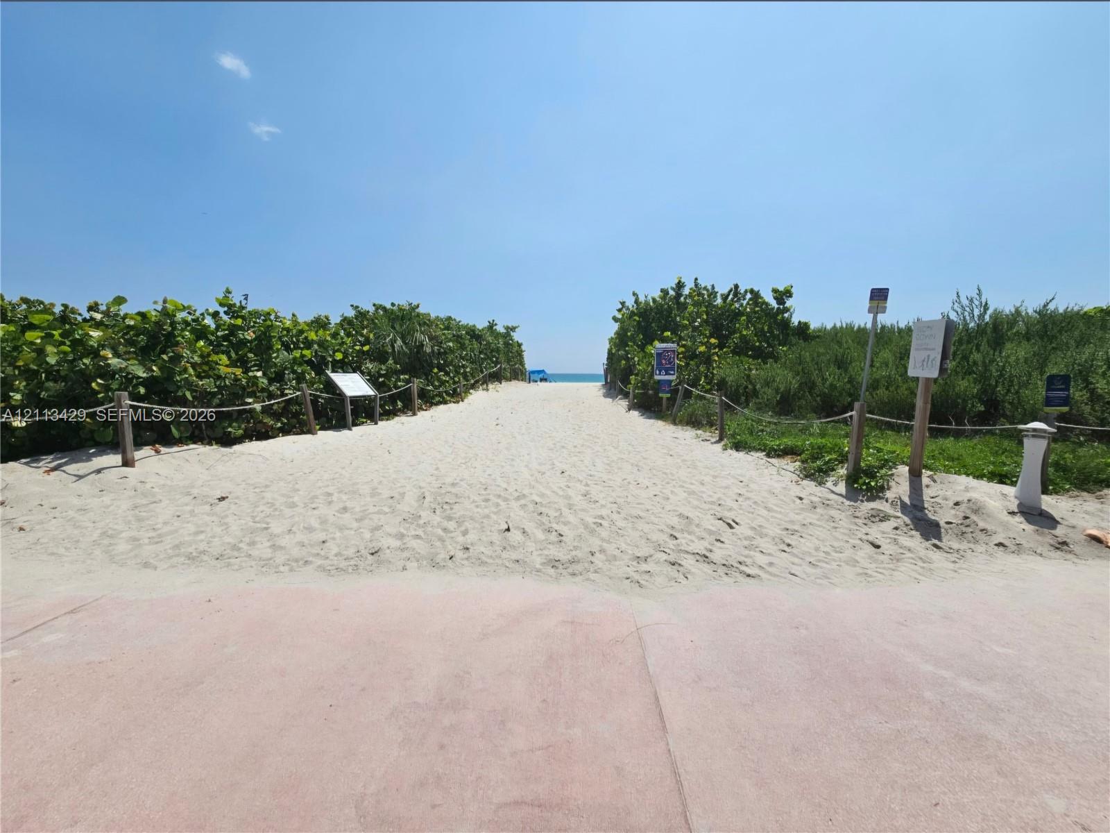 Sandy path access featuring a paved approach, natural vegetation border, and rope fencing
