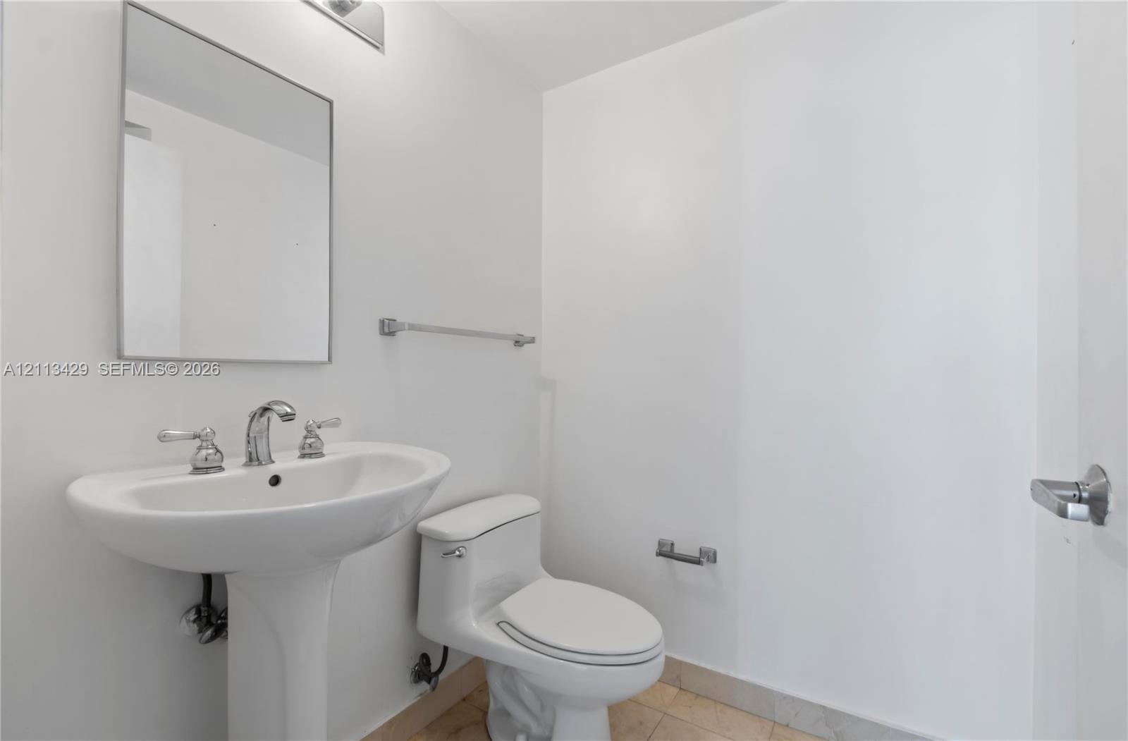 Pedestal sink with polished chrome widespread faucet, frameless wall mirror, chrome light fixture, and tile flooring