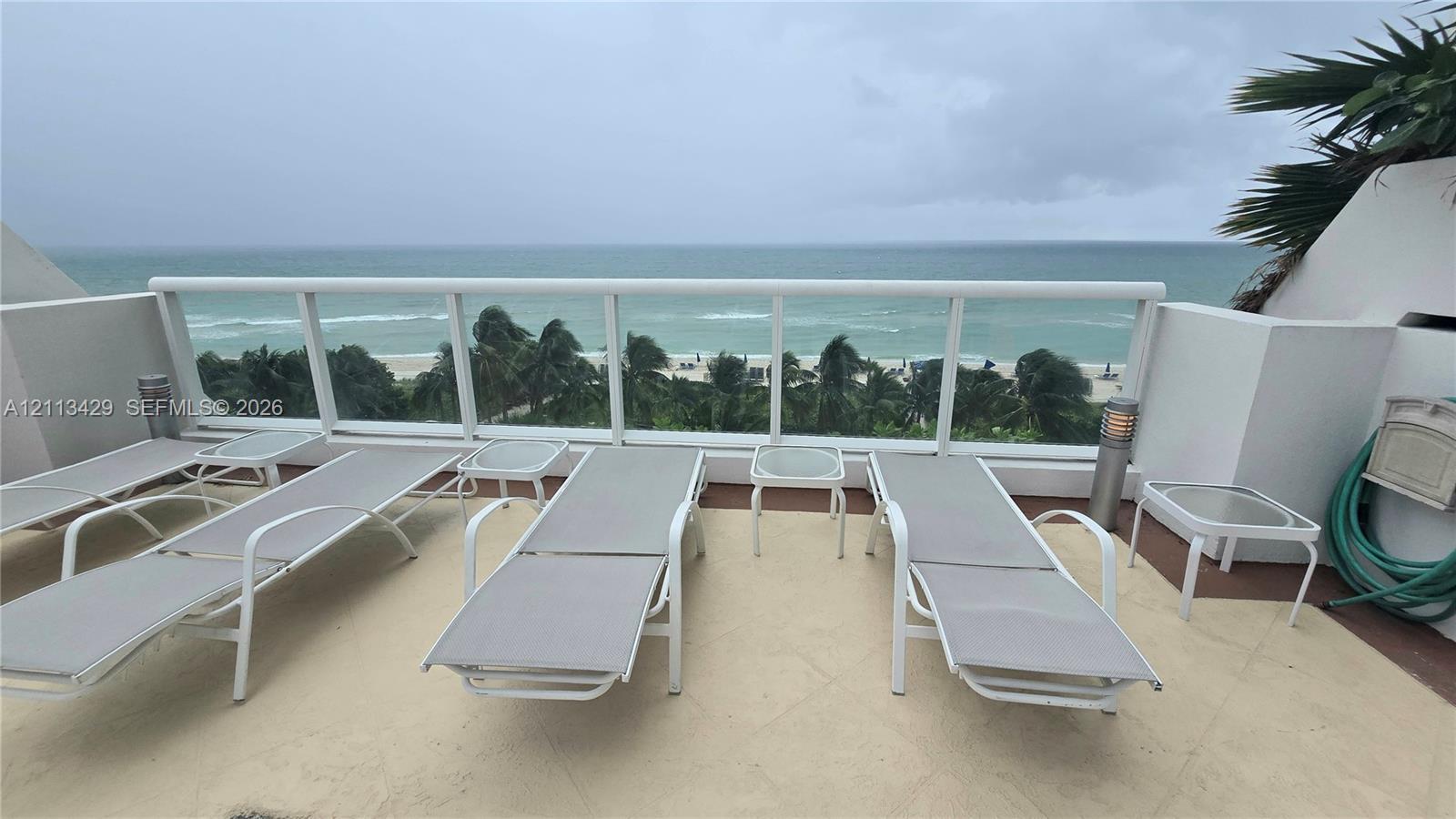 Private balcony with stone flooring, custom glass and white metal railing, and ocean backdrop