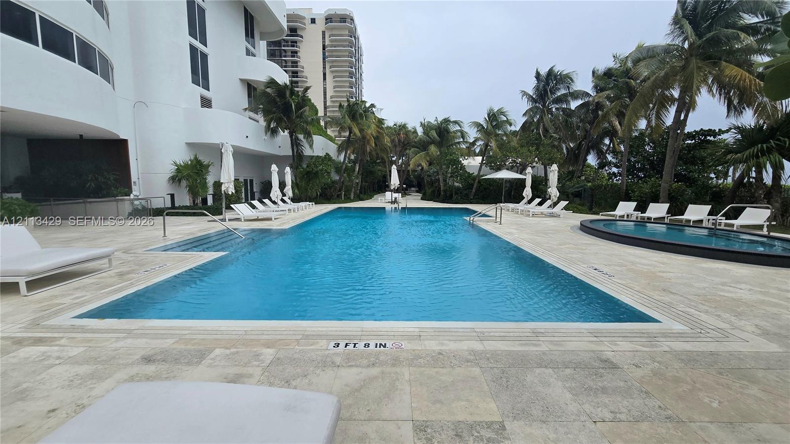 Swimming pool with stone-tiled deck, integrated lap lanes, secondary circular pool, and tropical palm tree landscaping