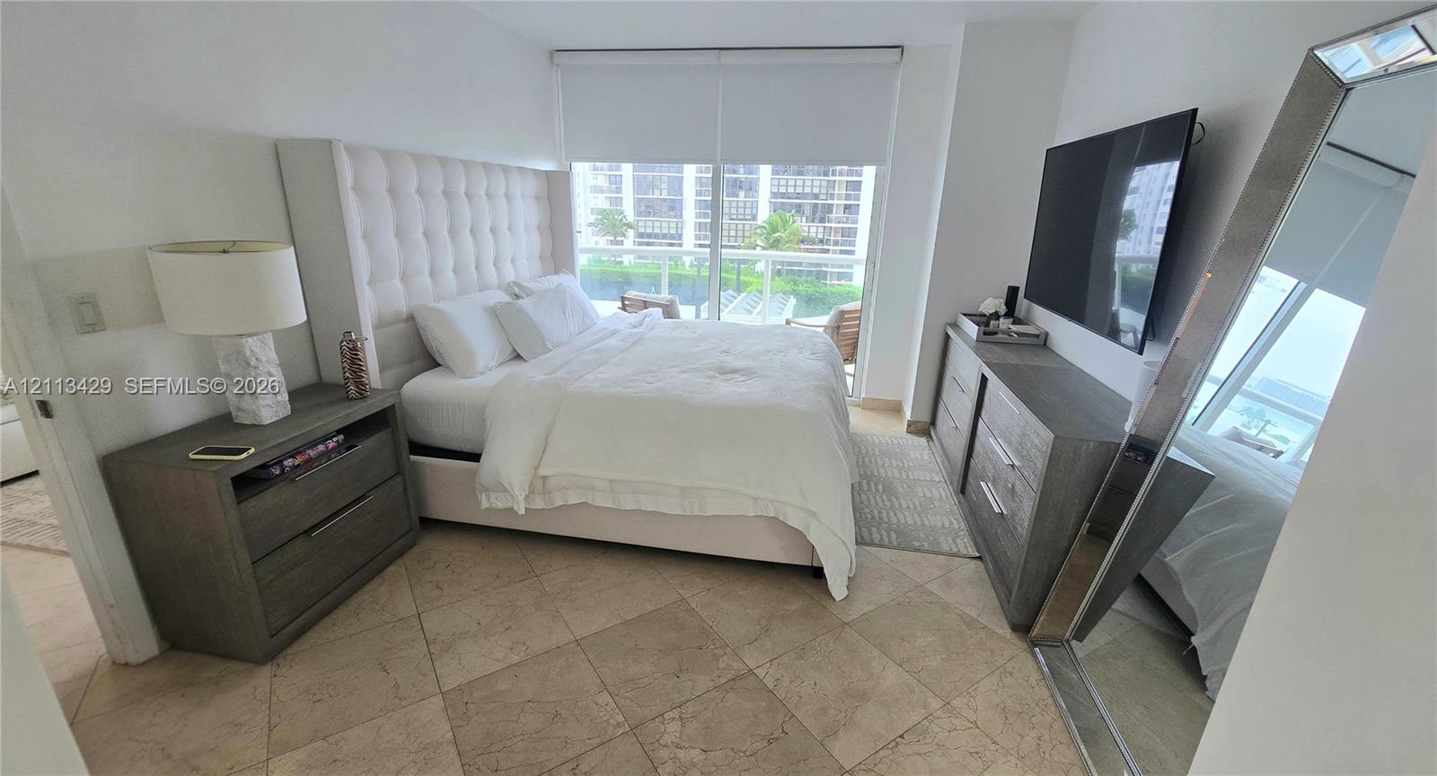 Spacious room featuring neutral stone tile flooring, floor-to-ceiling glass sliding doors, and a private balcony