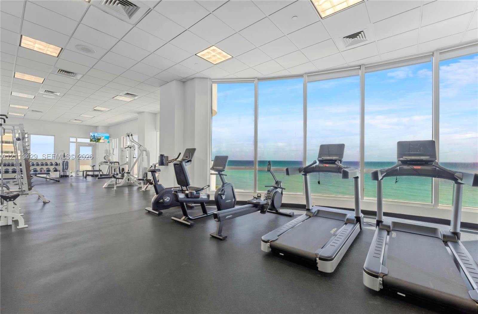 Fitness center featuring floor-to-ceiling windows, panoramic ocean scenery, recessed ceiling lighting, and resilient rubber flooring