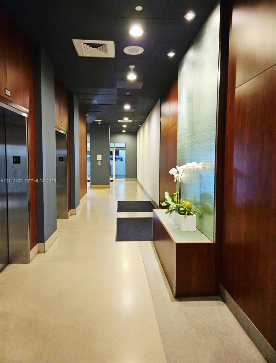 Hallway featuring polished concrete flooring, full-height wood-finish wall paneling, recessed ceiling lighting, and a built-in illuminated decorative accent wall