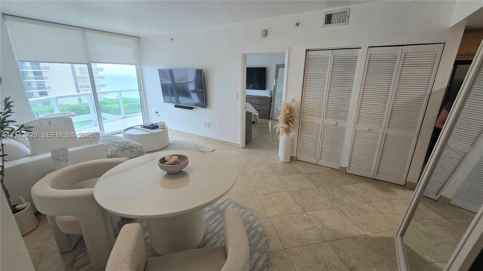 Living area featuring floor-to-ceiling windows, natural stone tile flooring, dual sets of louvered-panel closet doors, and a glass-railed balcony