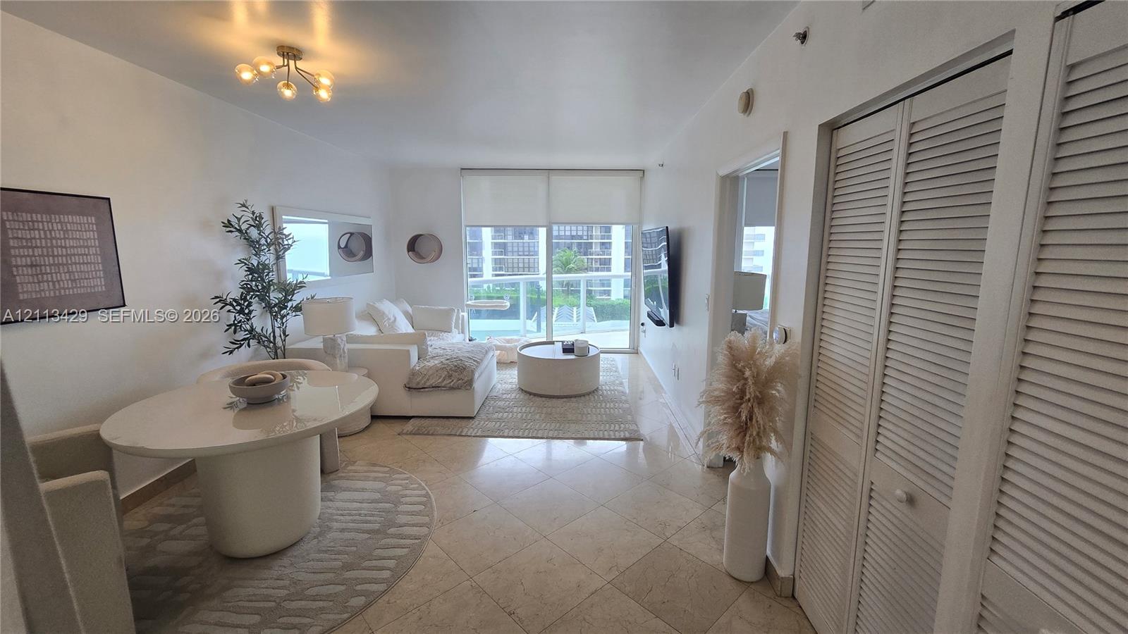 Living area featuring large-format tile flooring, louvered-style closet doors, glass sliding doors, and a multi-bulb flush-mount light fixture