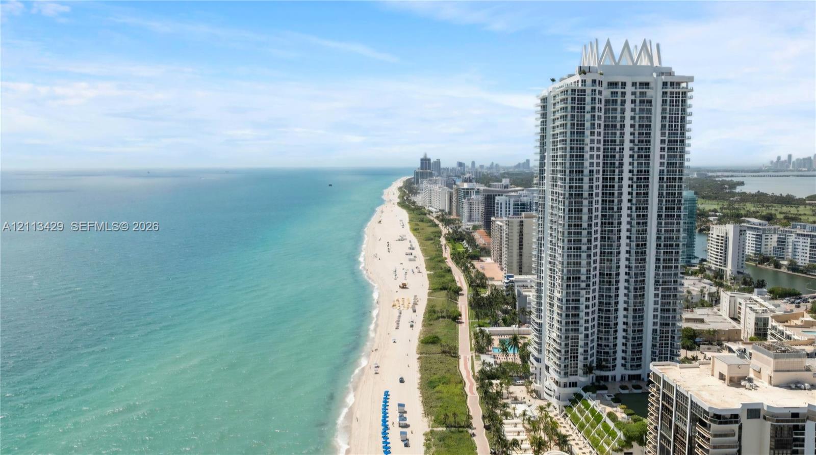 High-rise residential tower featuring a multi-story exterior, glass balconies, tiered architectural crown, and direct shoreline proximity