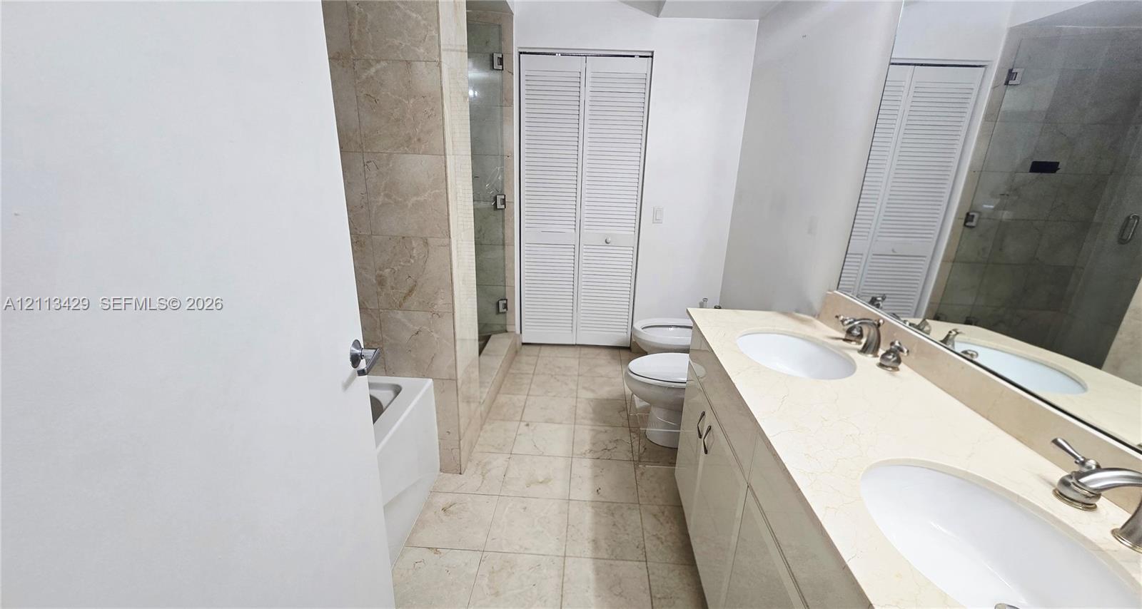 Bathroom featuring a dual-sink vanity with a stone countertop, a glass-enclosed shower, a soaking tub, and louvered bifold closet doors