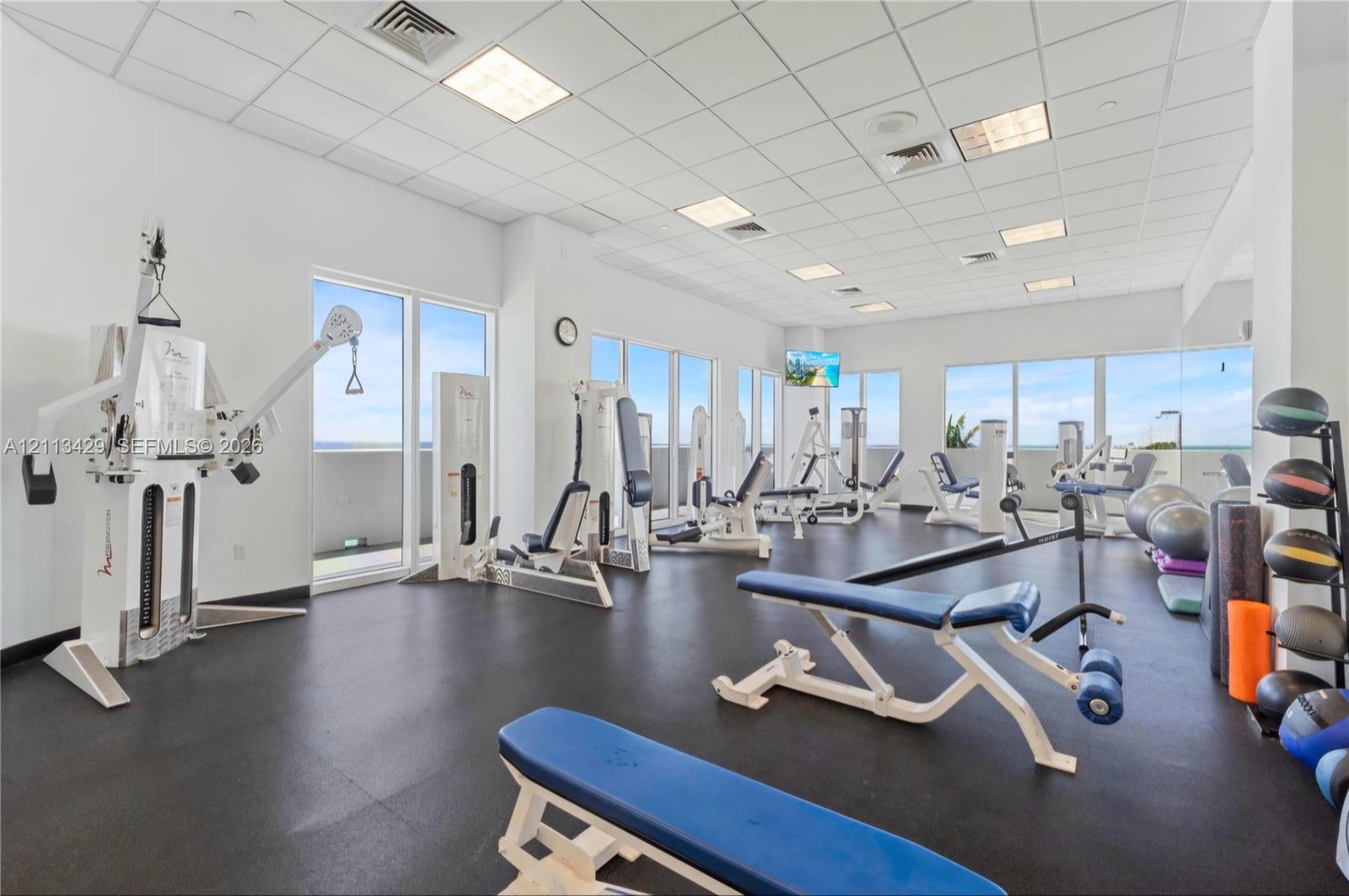 Fitness center featuring rubber flooring, recessed drop ceiling lighting, and expansive floor-to-ceiling windows