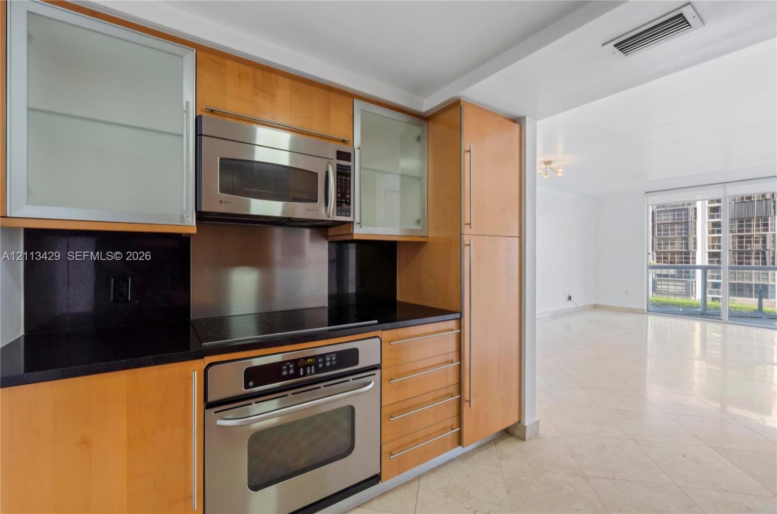 Kitchen featuring flat-panel wood cabinetry, black countertops, stainless steel appliances, and glass-front upper cabinet doors