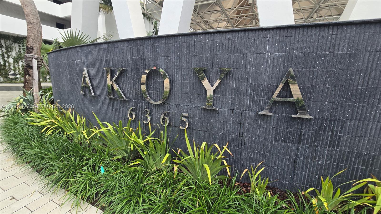 Curved wall finished in stacked charcoal stone featuring polished metal dimensional lettering, numeric address signage, and a manicured foundation landscape