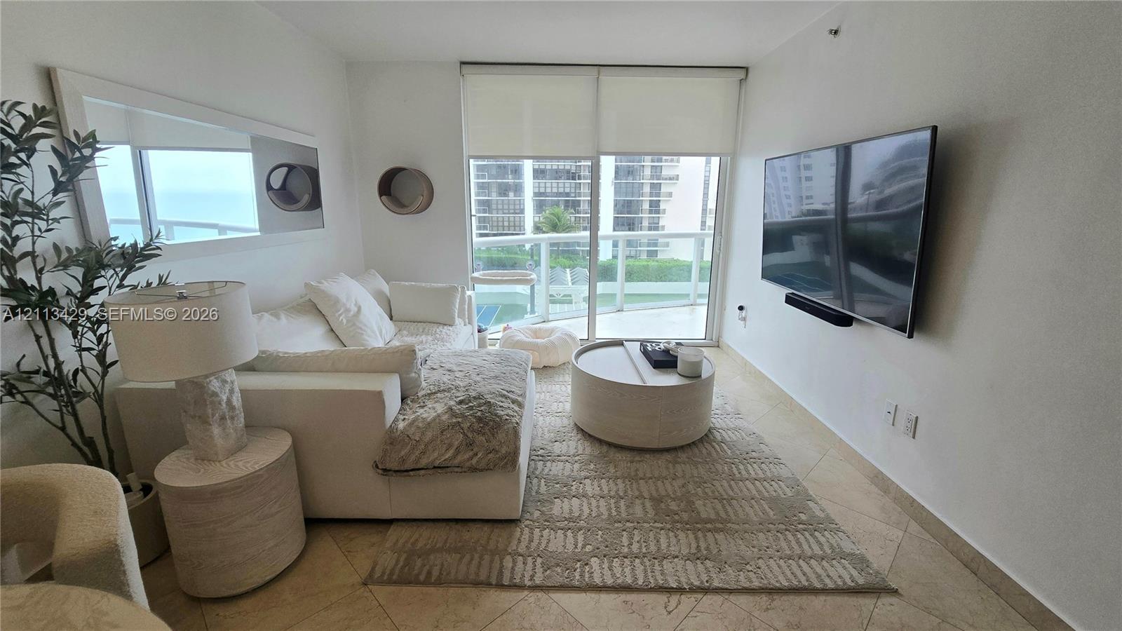 Living space featuring stone-finish tile flooring, wall-mounted television, floor-to-ceiling sliding glass doors, and a private balcony with glass railing