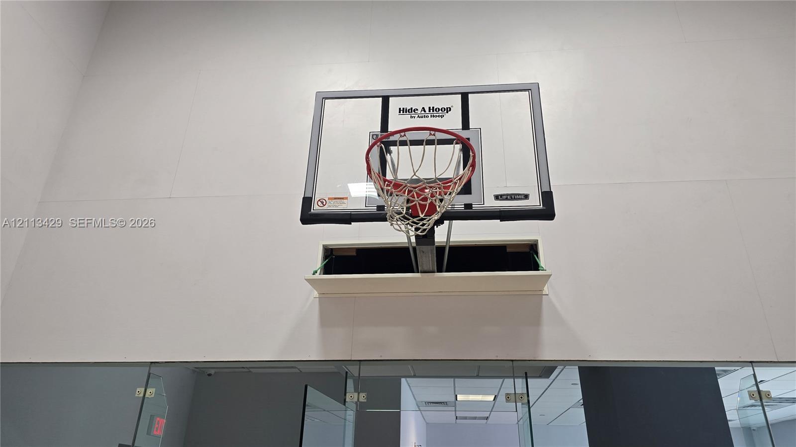 Retractable wall-mounted basketball hoop with a clear polycarbonate backboard and orange steel rim