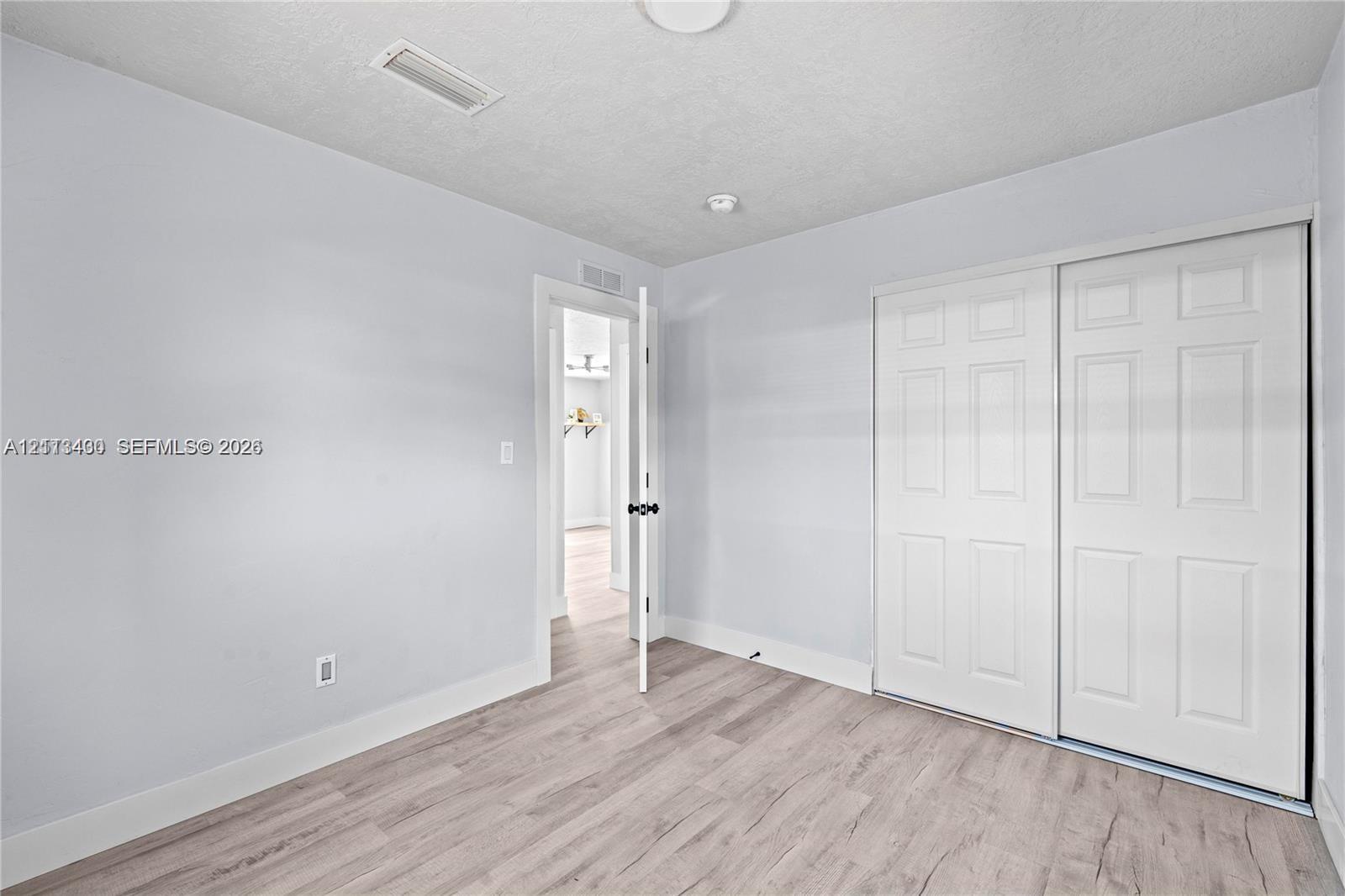 Neutral-toned room featuring wood-finish flooring, a double-panel sliding closet, and a white interior door with a matte black handle