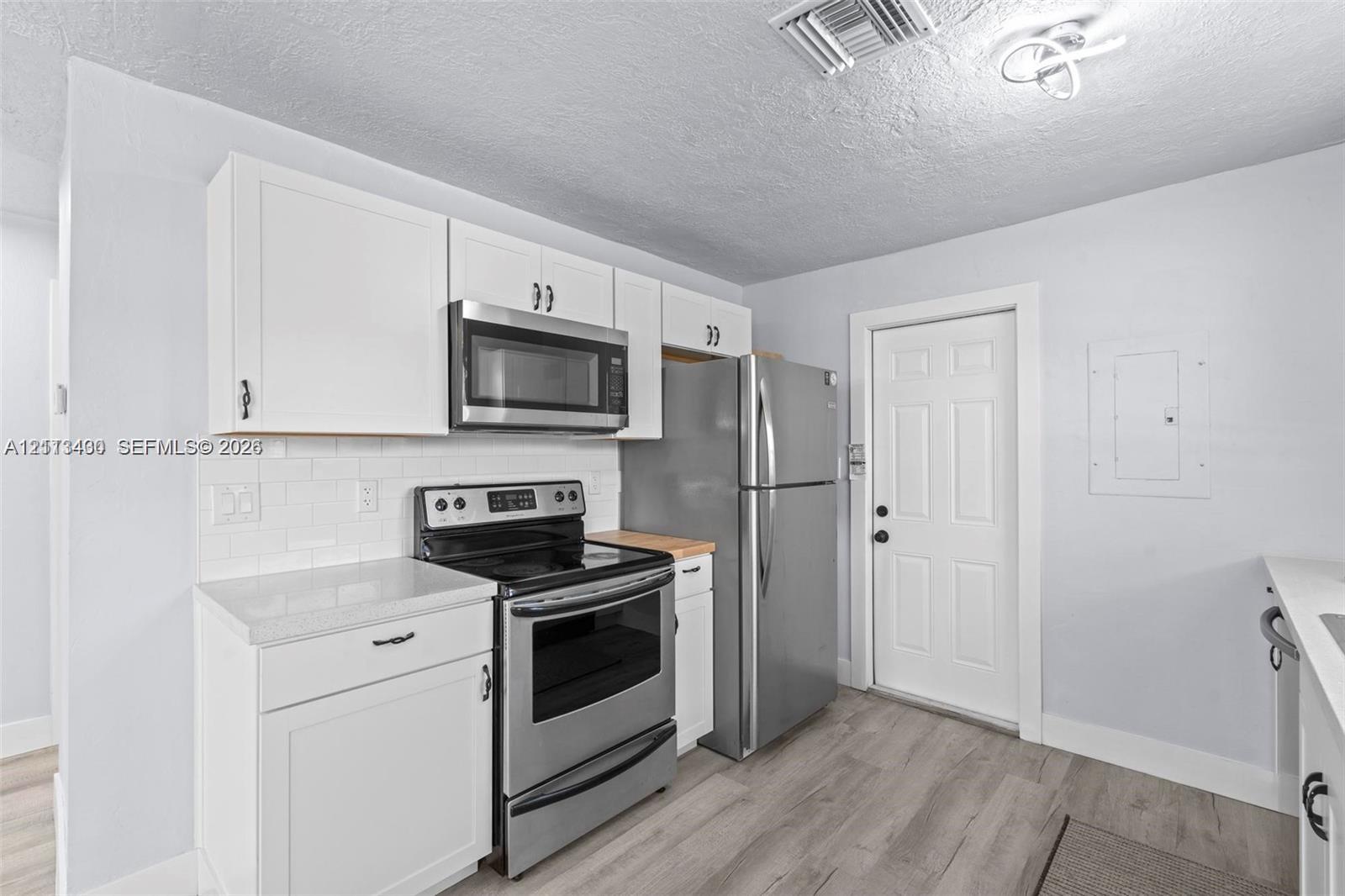 Kitchen featuring white cabinetry, subway tile backsplash, wood-finish flooring, and stainless steel appliances