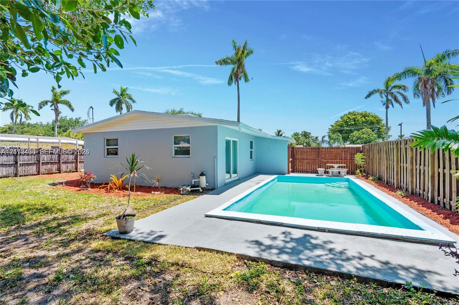 Rear exterior featuring a rectangular inground swimming pool, concrete pool deck, wood-style privacy fencing, and exterior landscape beds