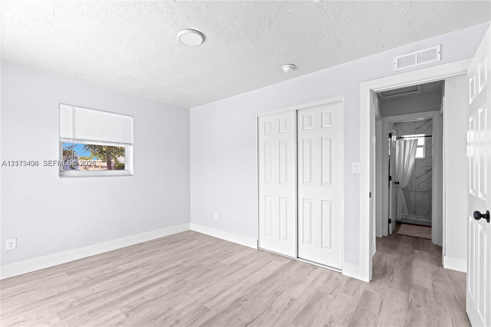 Wood-finish flooring, white paneled closet doors, and window with horizontal blinds