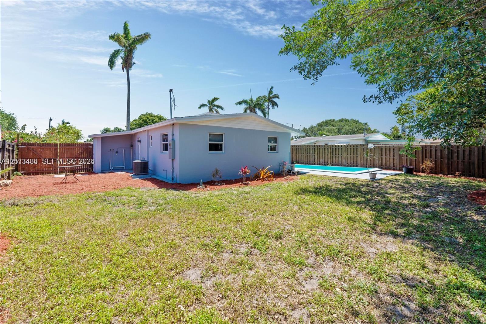 Private backyard featuring an in-ground swimming pool, concrete pool deck, enclosed perimeter wood fencing, and mature palm trees