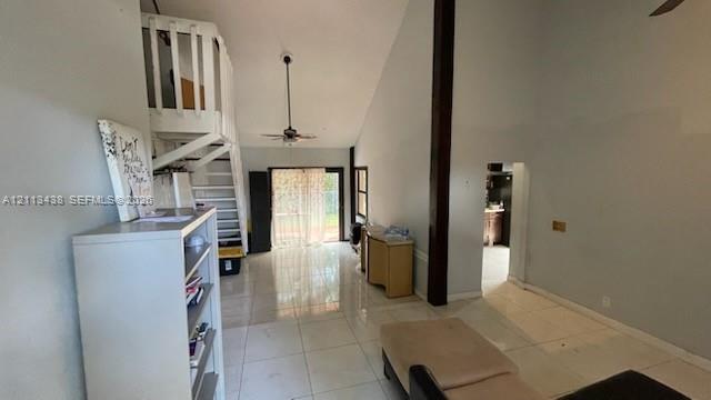 Vaulted ceilings featuring a dark wood-finish structural beam, tile flooring, and an open staircase with white wood-finish railings