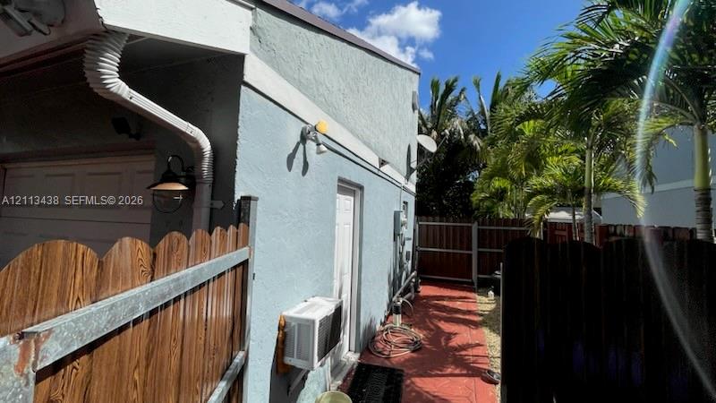 Stucco exterior featuring an attached garage, a side entry door, exterior wall-mounted lighting, and a fenced side yard with paved walkway