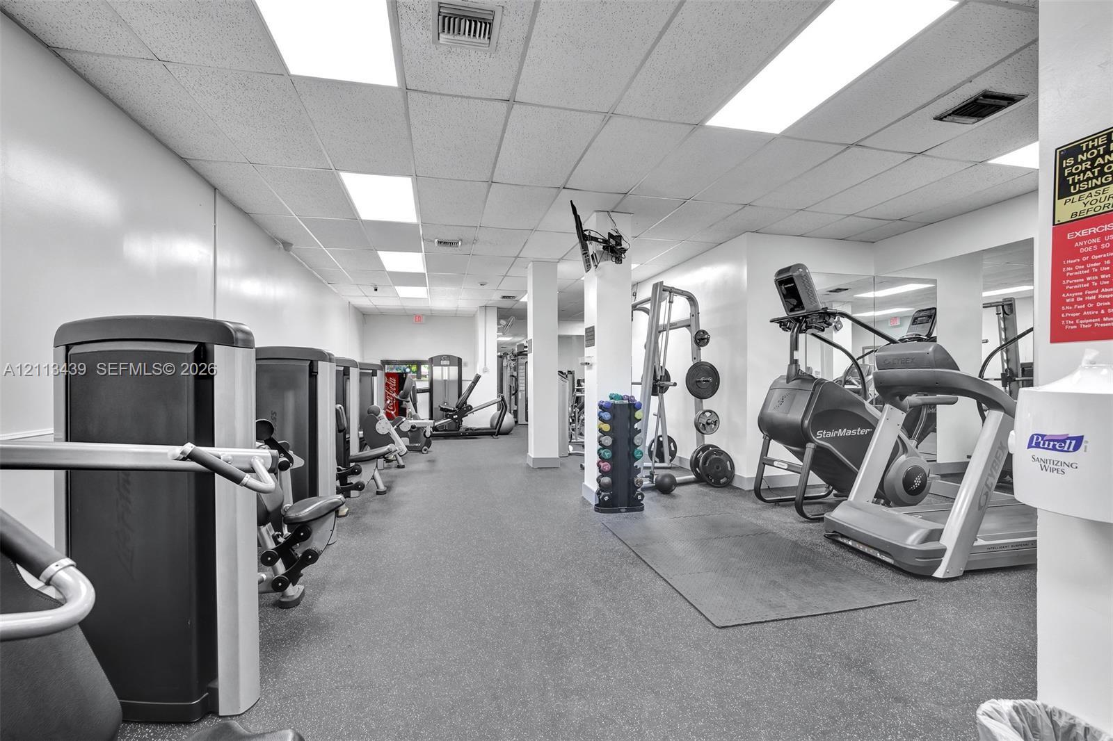 Fitness room featuring rubberized flooring, recessed fluorescent lighting, and mirrored wall panels