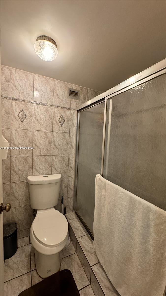Full-height tiled walls featuring decorative diamond-patterned inserts, walk-in shower with a glass door, ceramic tile flooring, and a flush-mount ceiling light fixture