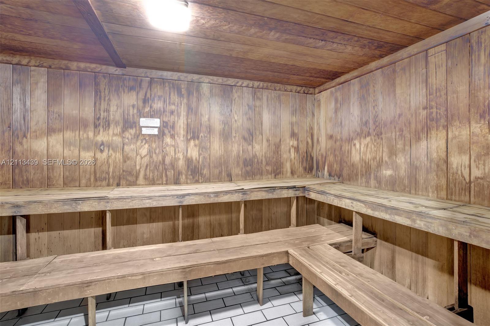 Sauna featuring wood-paneled walls and ceiling, multi-level built-in wood bench seating, and tile flooring