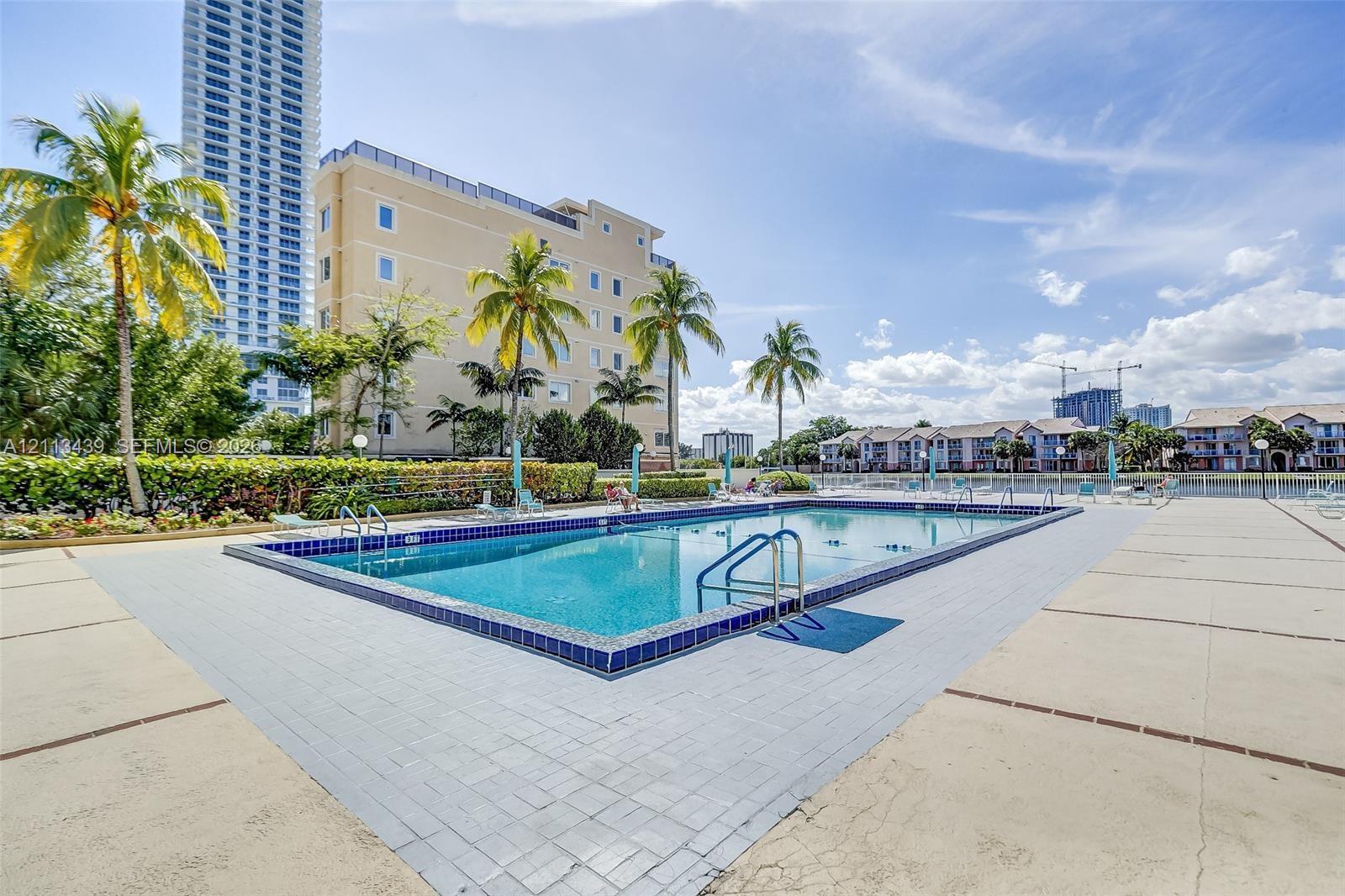 Swimming pool featuring tile trim, metal handrails, and a surrounding paved deck with mature palm trees