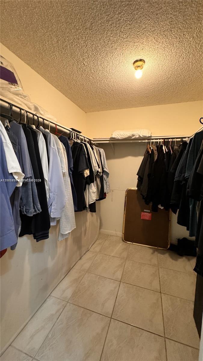 Storage space featuring built-in shelving, hanging rods, and neutral-tone tile flooring