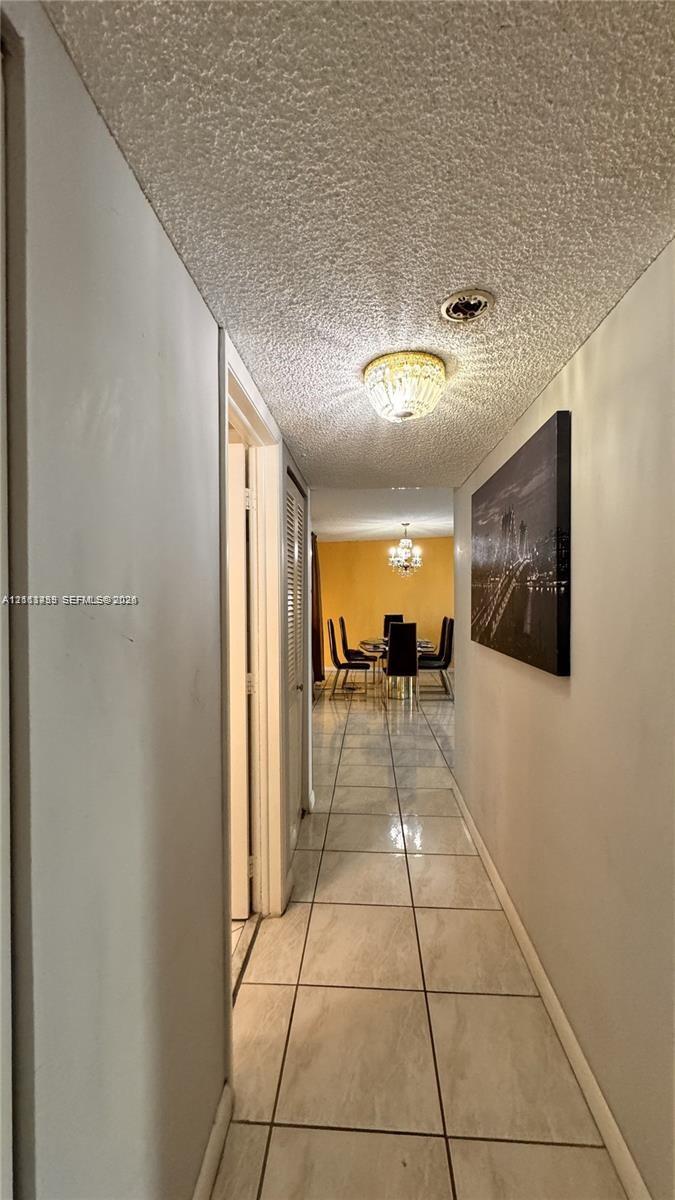 Hallway featuring large-format ceramic tile flooring, textured ceiling, flush-mount decorative lighting, and louvered closet doors