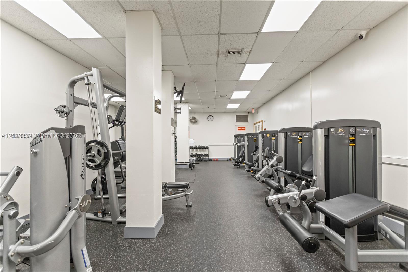 Fitness space featuring rubberized flooring, structural columns, and recessed panel lighting