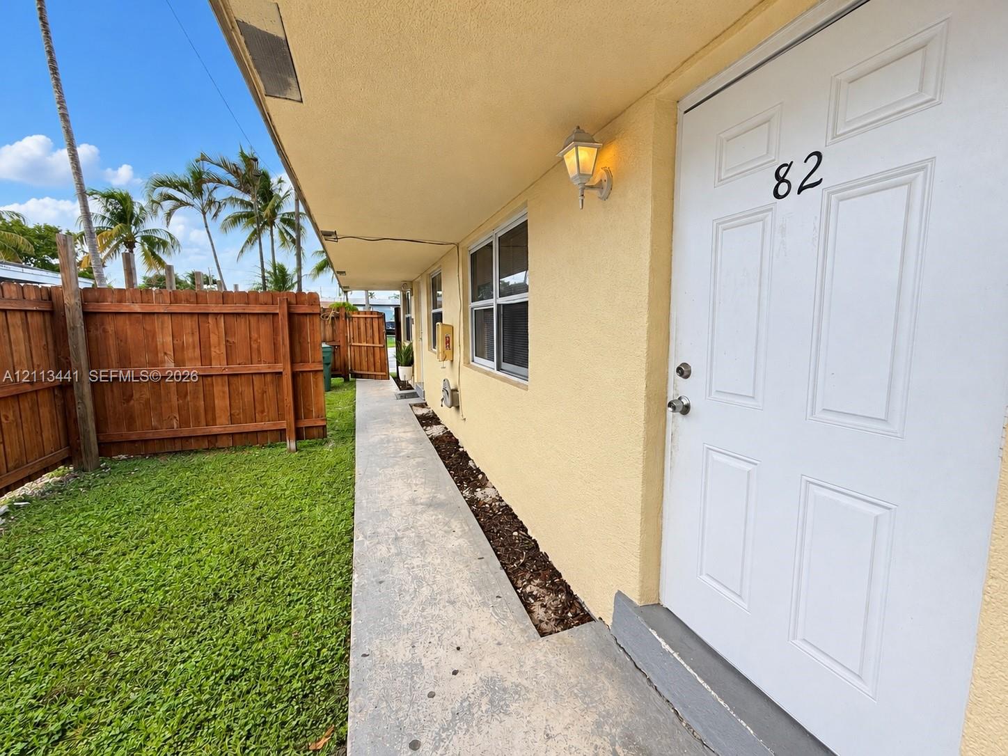 Exterior walkway with concrete paving, wood privacy fencing, and an attached outdoor sconce