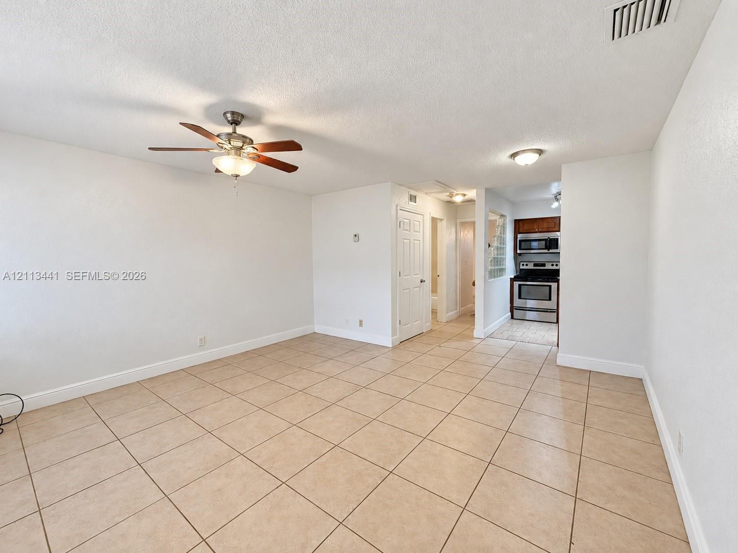 Open-concept interior featuring large-format neutral tile flooring, ceiling fan with integrated light fixture, recessed lighting, and kitchen equipped with stainless steel appliances