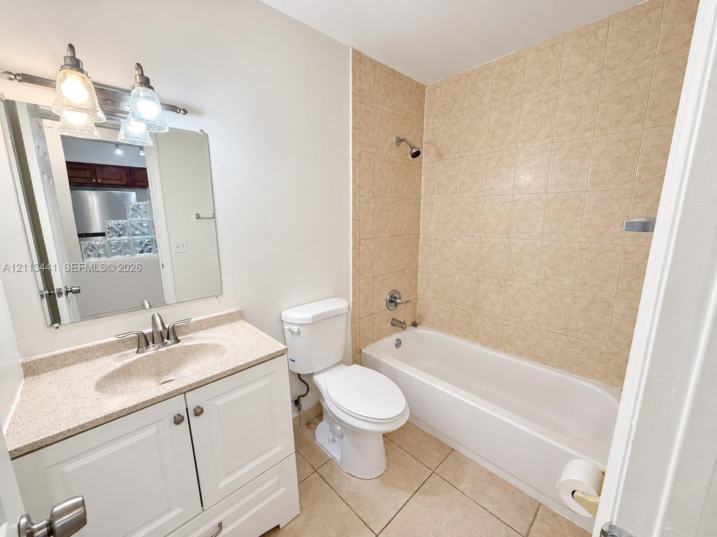 Bathroom featuring white vanity cabinetry with a solid surface countertop, integrated sink, tile-surround shower-tub combination, and neutral-tone tile flooring