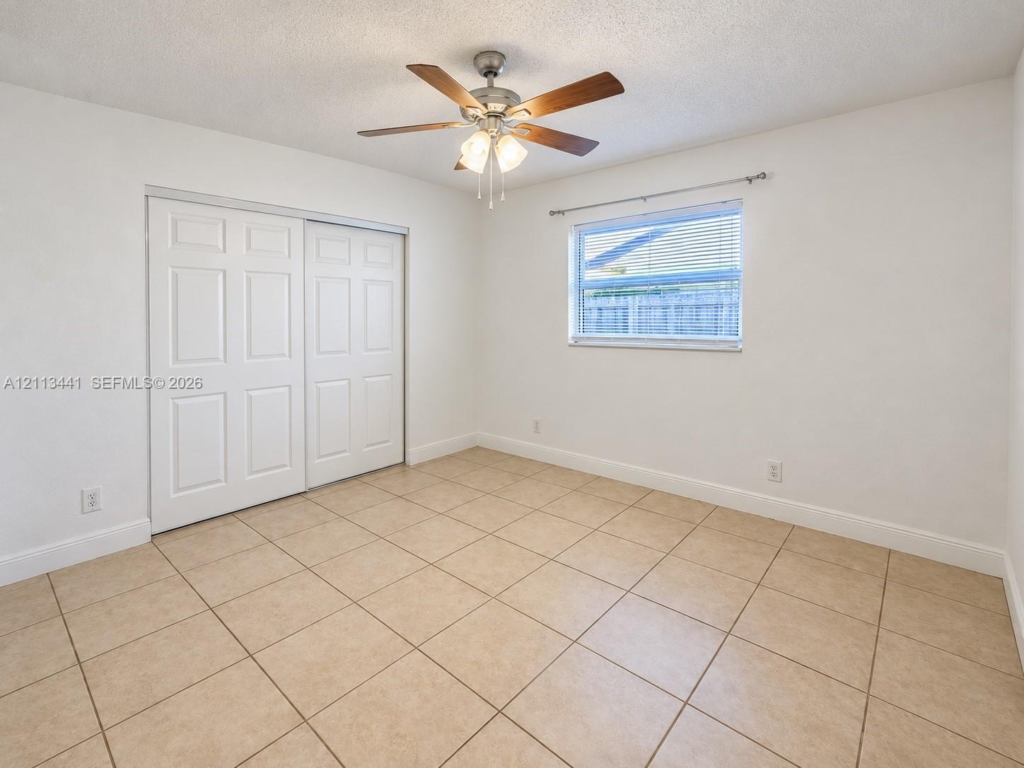 Tile flooring, dual-panel sliding closet doors, ceiling fan with integrated lighting, and window with installed curtain rod