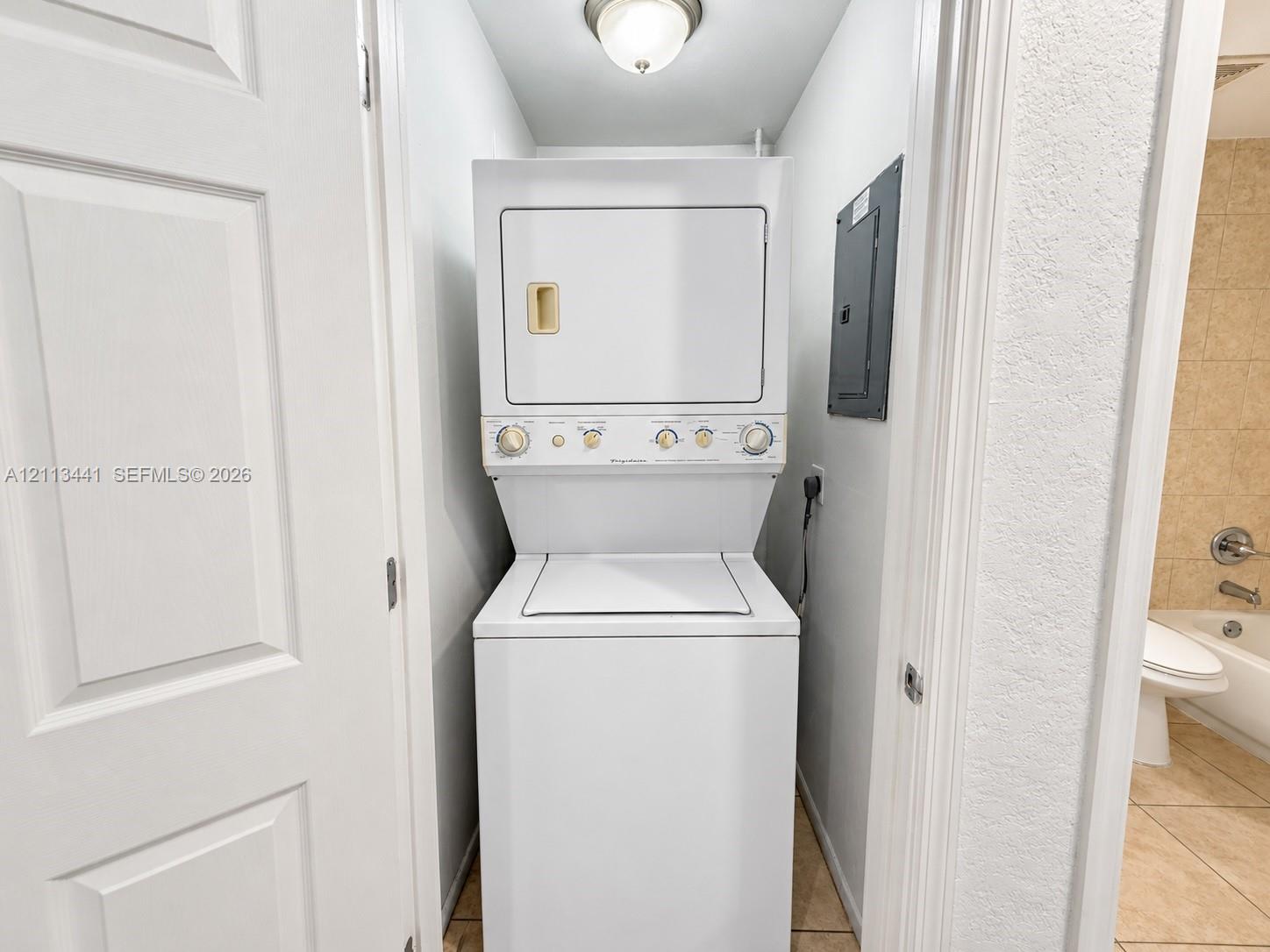 Stackable laundry center featuring a top-loading washer and front-loading dryer, flush-mount ceiling light fixture, and tile flooring