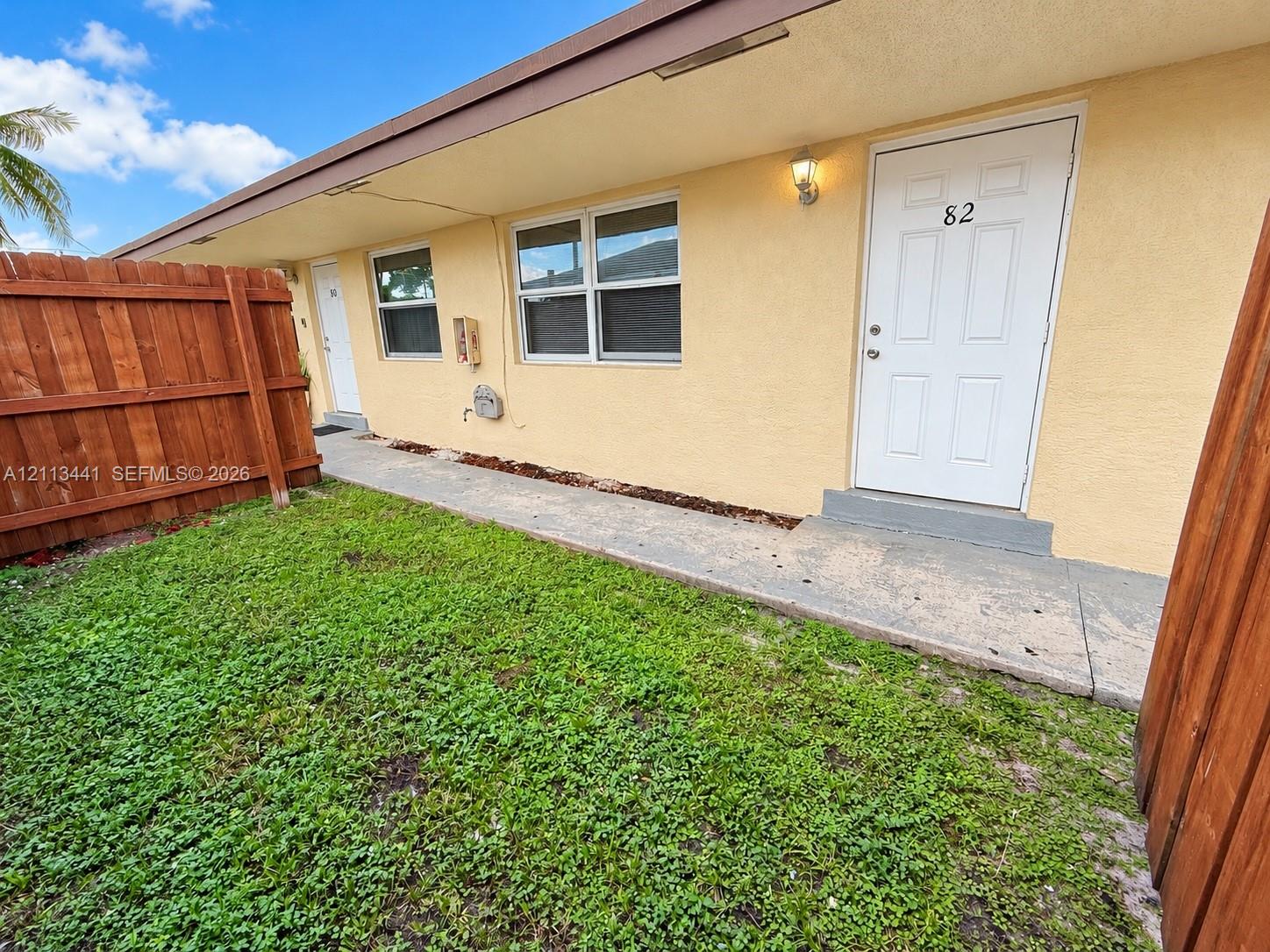 Stucco exterior featuring dual-pane windows, wood-style privacy fencing, and a concrete walkway