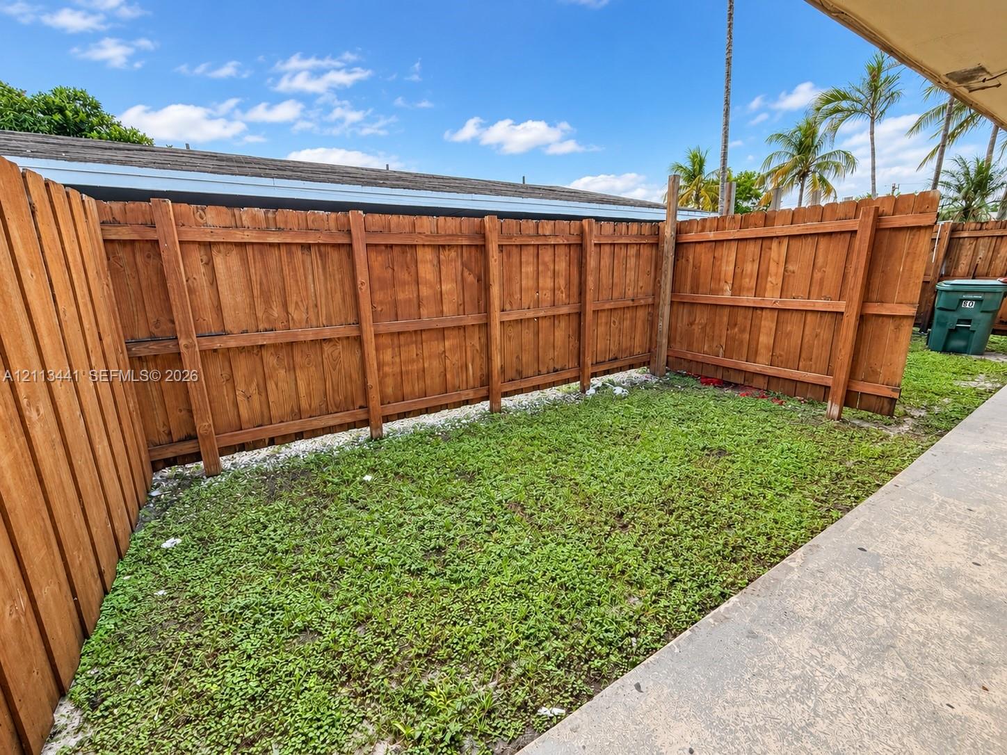 Outdoor space featuring a concrete patio, wood privacy fencing, and a grass lawn